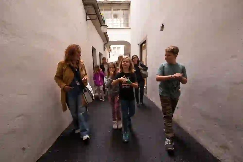 Eine Gruppe fröhlicher Kinder folgt der lächelnden Stadtführerin durch eine enge Gasse. Die Mischung aus Neugier und Vergnügen prägt die Atmosphäre.