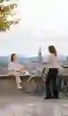 Zwei Frauen unterhalten sich im Rosengarten in Bern, die eine sitzt auf der Mauer, die andere steht mit ihrem Fahrrad daneben. Sie geniessen die Aussicht auf die Stadt mit dem Berner Münster im Hintergrund, eingebettet in die friedvolle Stimmung eines Tages im Frühling. Die Szene ist geprägt von Gelassenheit und der Schönheit des Moments.