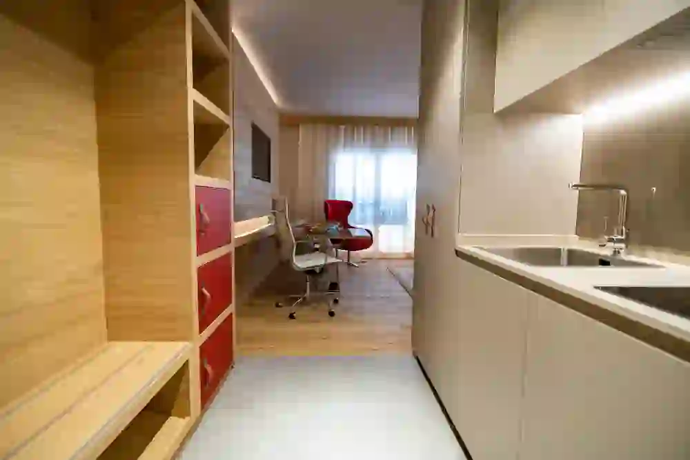 La photo montre une chambre au design moderne à Los Lorentes Residences, avec une combinaison harmonieuse d'éléments naturels en bois et de touches de couleur. Un coin lecture confortable avec une chaise rouge invite à la détente.