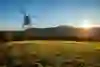 L'immagine mostra un piccolo elicottero che si libra su un prato idilliaco nel bagliore dorato del sole serale. Sullo sfondo si estende una catena di colline e il sole è appena prima dell'orizzonte, creando un gioco di luce rilassante che immerge la scena in un bagliore caldo e luminoso.