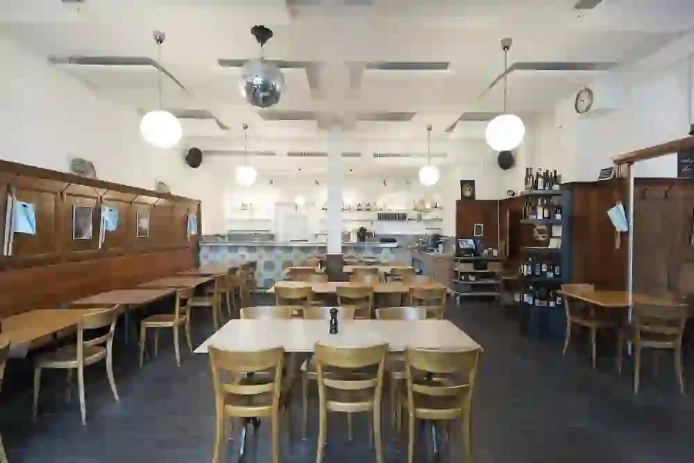 Ein leeres, helles Restaurant mit Holztischen und einer Discokugel, das eine Atmosphäre von entspannter Alltagstauglichkeit und potenziellem Vergnügen ausstrahlt.