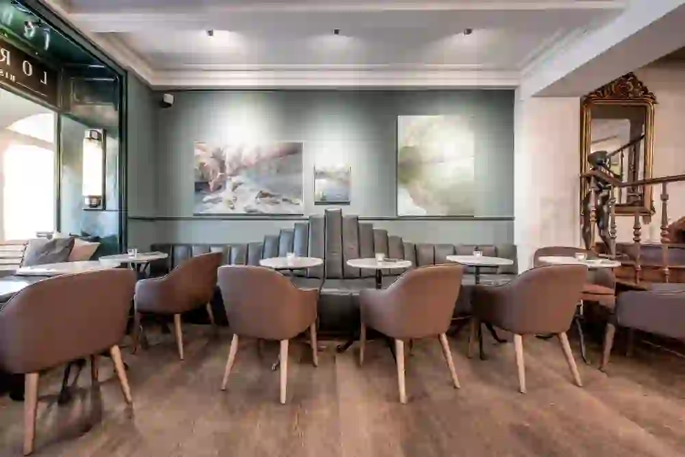 Elegante, ruhige Ecke des Lorenzini mit Kunstwerken, grünen Wänden, Ledersitzen und Spiegel, die eine kultivierte, entspannende Atmosphäre schaffen.