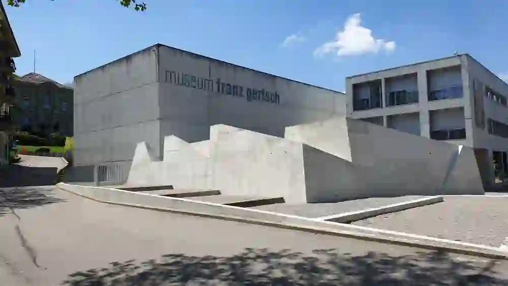 The Franz Gertsch Museum in Burgdorf presents itself as a modern building made of concrete, whose clear lines and geometric shapes radiate a calm, almost meditative atmosphere. In contrast to the traditional building in the background, it conveys an impression of contemporary elegance and artistic simplicity.