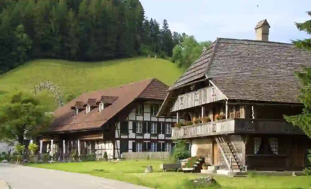 Traditionelle Schweizer Bauernhäuser mit charakteristischen Holzfassaden und Blumenkästen stehen im Heimatmuseum Trubschachen. Die grünen Hügel im Hintergrund unterstreichen das idyllische und ruhige Ambiente, das Einblicke in die ländliche Geschichte bietet.