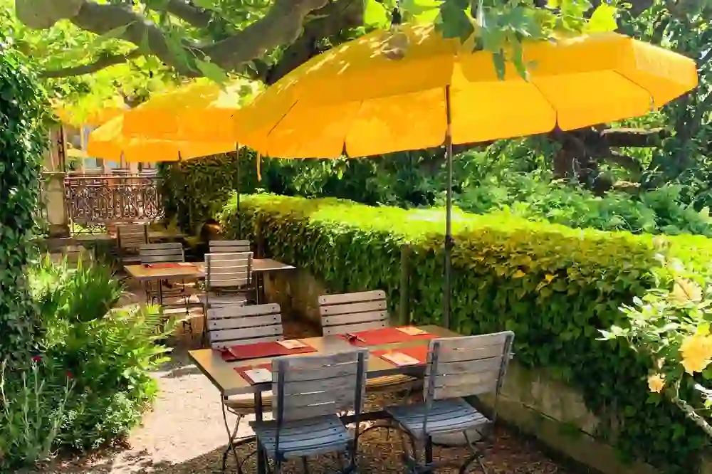 The photo shows a charming outdoor terrace of the Veranda restaurant, surrounded by green plants and enlivened by the bright yellow of the parasols. The sun-drenched scene promises a relaxed and cheerful atmosphere.
