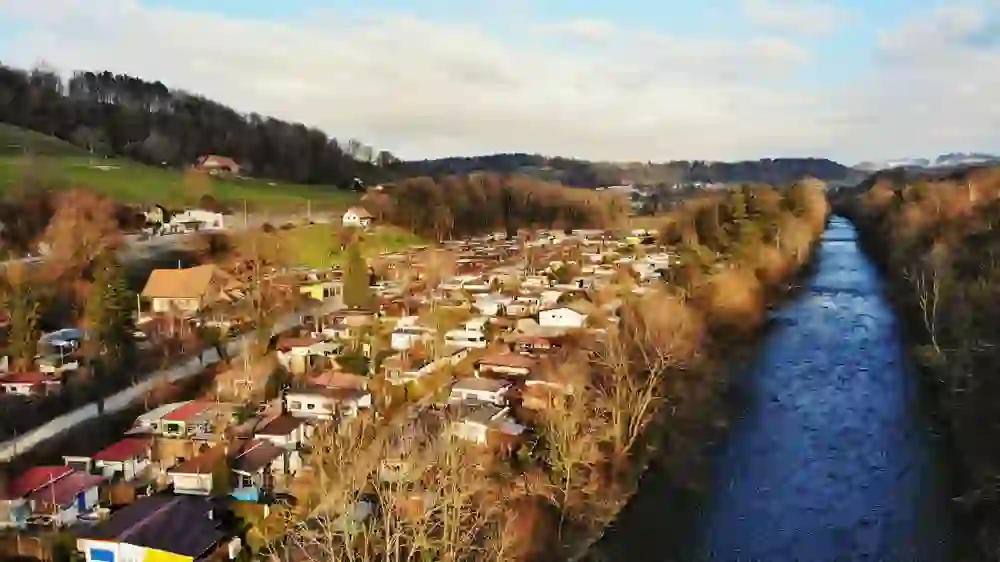 L'image montre une photo prise par une drosse du camping Thörishaus avec différentes cabanes de camping. A côté, on voit l'Aar bleu foncé et le camping est plongé dans une lumière dorée.