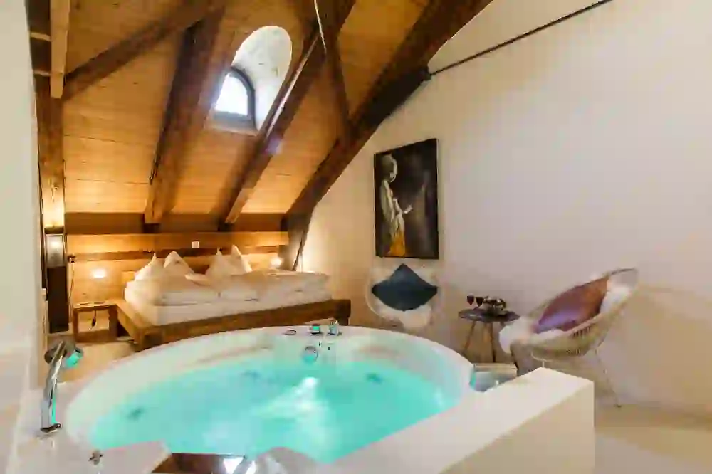 Das Bild zeigt ein luxuriöses Dachzimmer im Romantikhotel Bären Dürrenroth, ausgestattet mit einem grossen Whirlpool. Die warme Holzverkleidung und die sanfte Beleuchtung schaffen eine entspannende und romantische Stimmung.