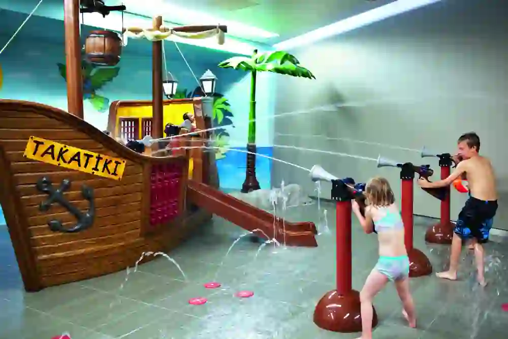 Kinder spielen im Kinderparadies Bernaqua und haben Spass beim Zielen mit Wasserpistolen, umgeben von einer lebendigen Dekoration, die an ein Piratenschiff erinnert.