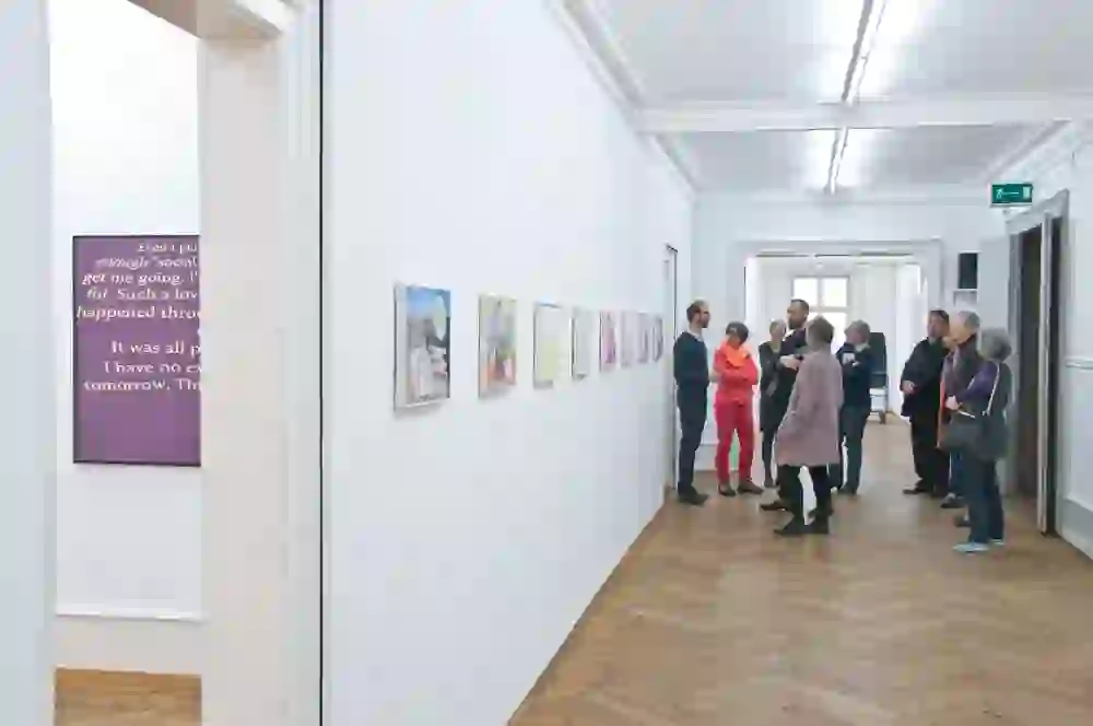 Das Foto zeigt eine Gruppe von Menschen in einer Kunstgalerie, anscheinend im Kunsthaus Langenthal. Sie scheinen in ein Gespräch über die ausgestellten Werke vertieft zu sein.