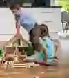 Das Bild zeigt zwei Kinder (ein Junge und ein Mädchen) beim Spielen mit einem Holz-Bauernhaus von Trauffer Holzspielwaren