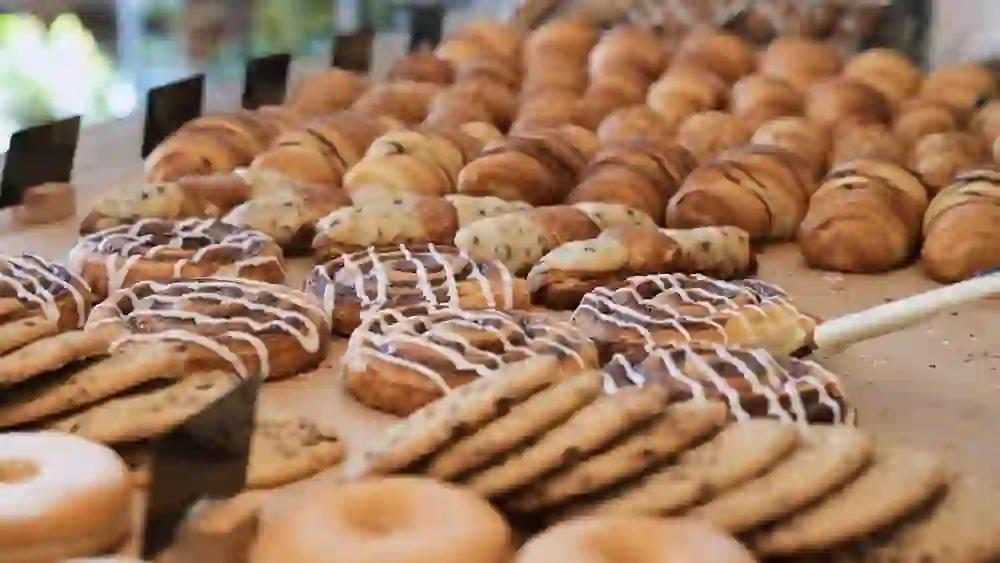 The picture shows a tantalising selection of pastries on a market stall. The freshly baked croissants, donuts and other sweet treats create an inviting and cheerful atmosphere, perfect for a cosy coffee break.