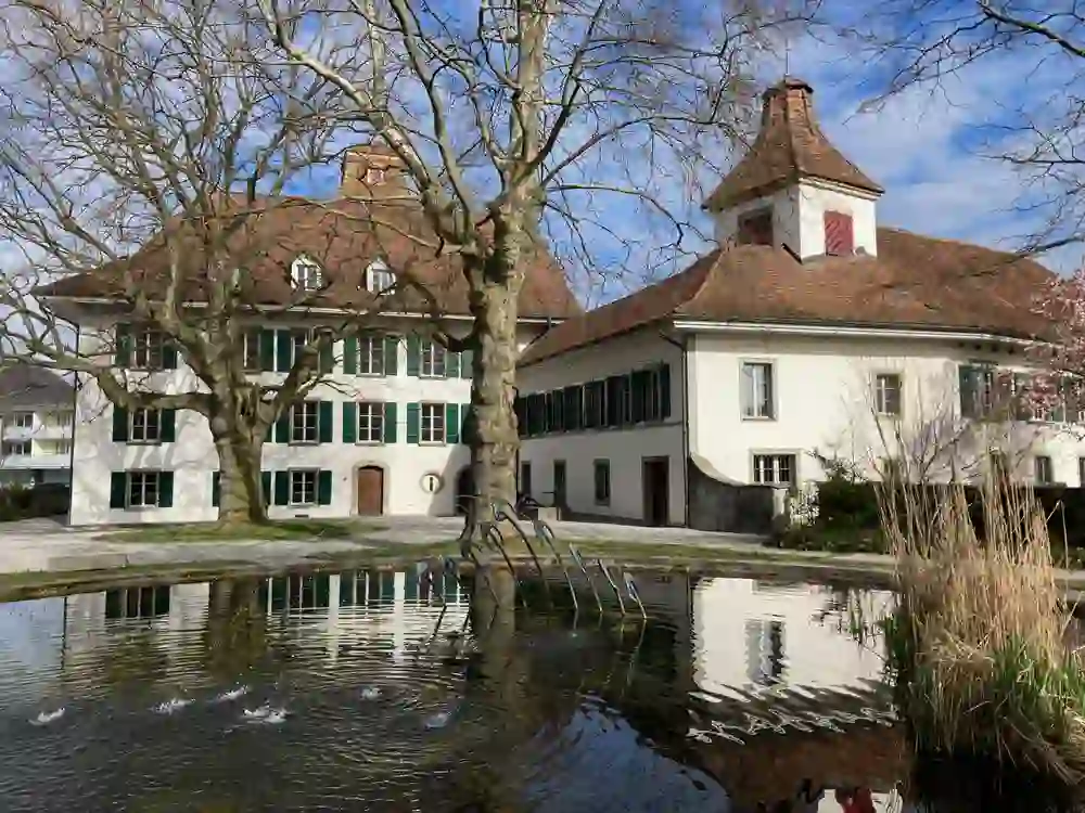 La photo montre le pittoresque château de Belp dans un environnement calme et clair. Le reflet du bâtiment classique dans l'eau devant lui crée une beauté symétrique et met en valeur l'architecture et le cadre idyllique.
