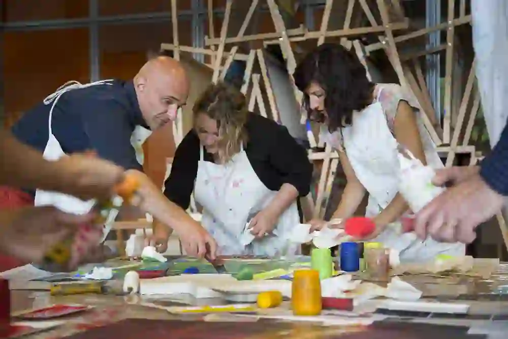 Kreative Konzentration und Zusammenarbeit in einem Workshop: Erwachsene und Kinder engagieren sich beim Malen, mit lebhaften Farbtöpfen und Werkzeugen, die leidenschaftlich verwendet werden.