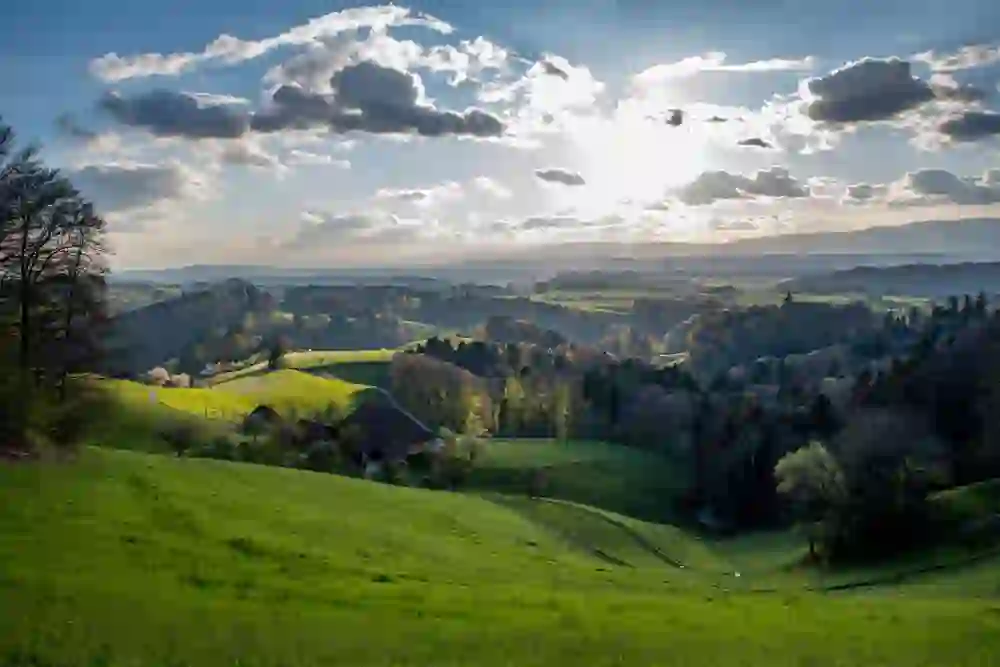 Das Bild fängt einen atemberaubenden Ausblick auf die Luftröhre Wäckerschwend ein, wo das goldene Sonnenlicht durch die Wolken bricht und die üppigen grünen Hügel erleuchtet.