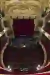 L'image capture le calme majestueux d'une salle de théâtre vide. De somptueuses loges ornées d'or encadrent les sièges en velours rouge qui attendent de prendre vie sur scène. Un lieu plein de drames et d'histoires potentiels.
