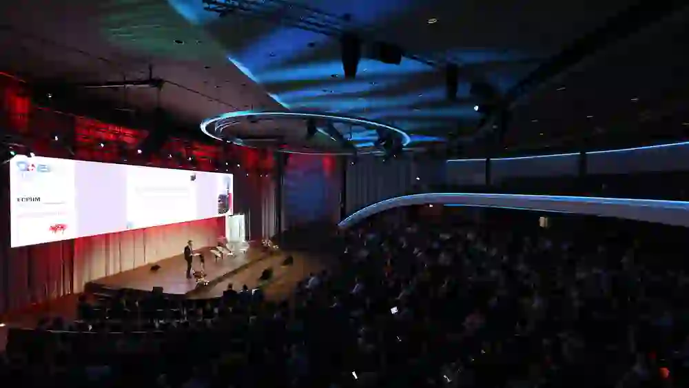 Weitläufiger Kongresssaal, gedämpftes Licht, konzentrierte Aufmerksamkeit. Eine ruhige, professionelle Atmosphäre mit feierlichem Charakter und internationalem Flair.