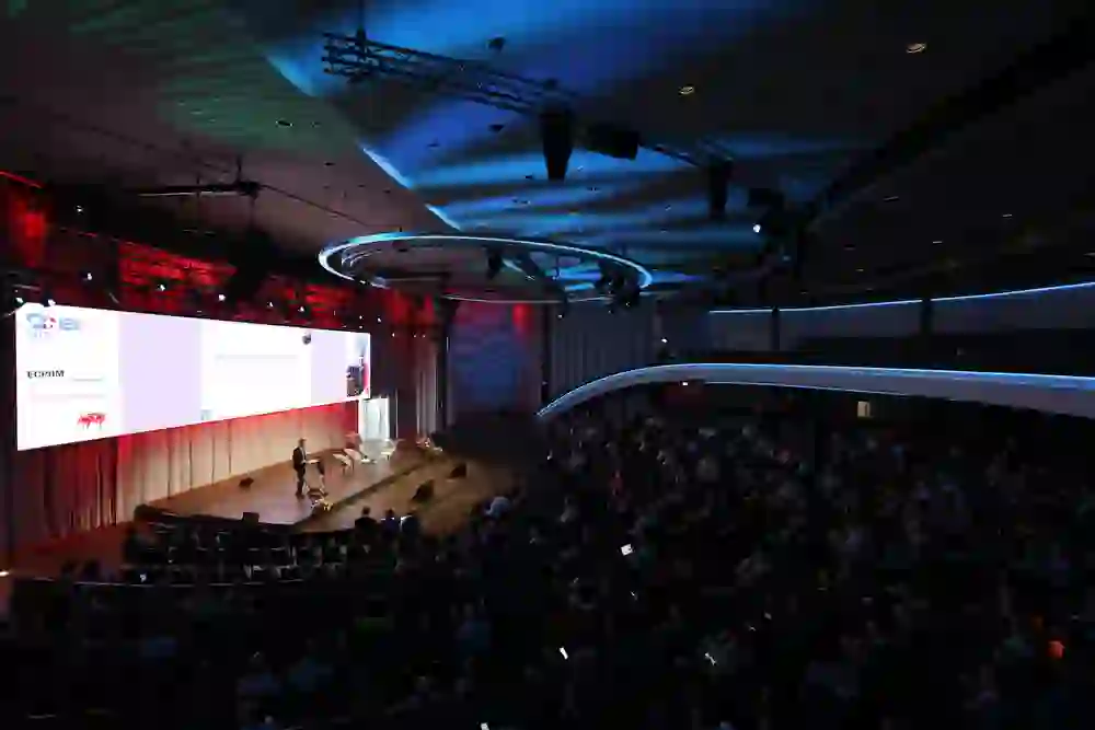 Vaste salle de congrès, lumière tamisée, attention concentrée. Une atmosphère calme et professionnelle au caractère solennel et à l'ambiance internationale.