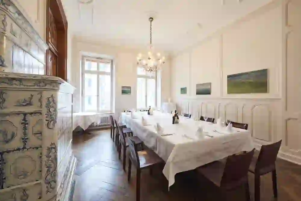 Der Salotto Siena im Ristorante Lorenzini in Bern versprüht eine Atmosphäre klassischer Eleganz. Ein prachtvoller Kachelofen dominiert den Raum, während natürliches Licht durch die grossen Fenster fällt und die kunstvollen Gemälde an den Wänden hervorhebt.