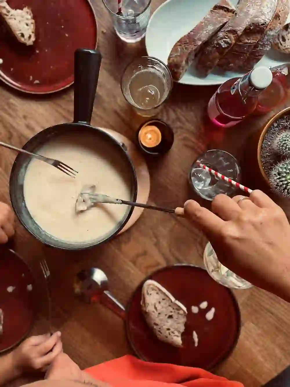 Das Bild zeigt ein geselliges Fondue-Essen, bei dem mehrere Hände Brotwürfel in den heißen, cremigen Käse tauchen. Die warme Atmosphäre und die gemeinsame Freude am Essen spiegeln sich in der gemütlichen Tischszene wider, die ein Gefühl von Zusammengehörigkeit vermittelt.