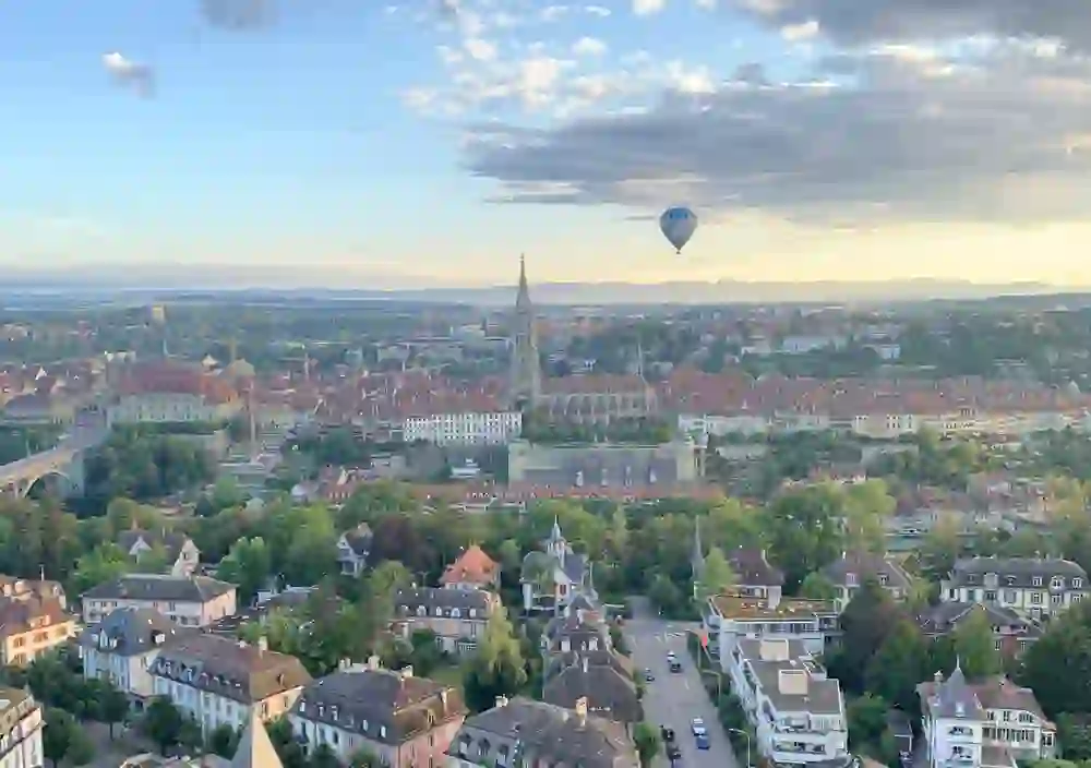 A hot-air balloon glides over the rooftops of Bern, which glow in the warm evening light. The city seems peaceful, vast and almost fairytale-like - a moment full of lightness and quiet beauty.