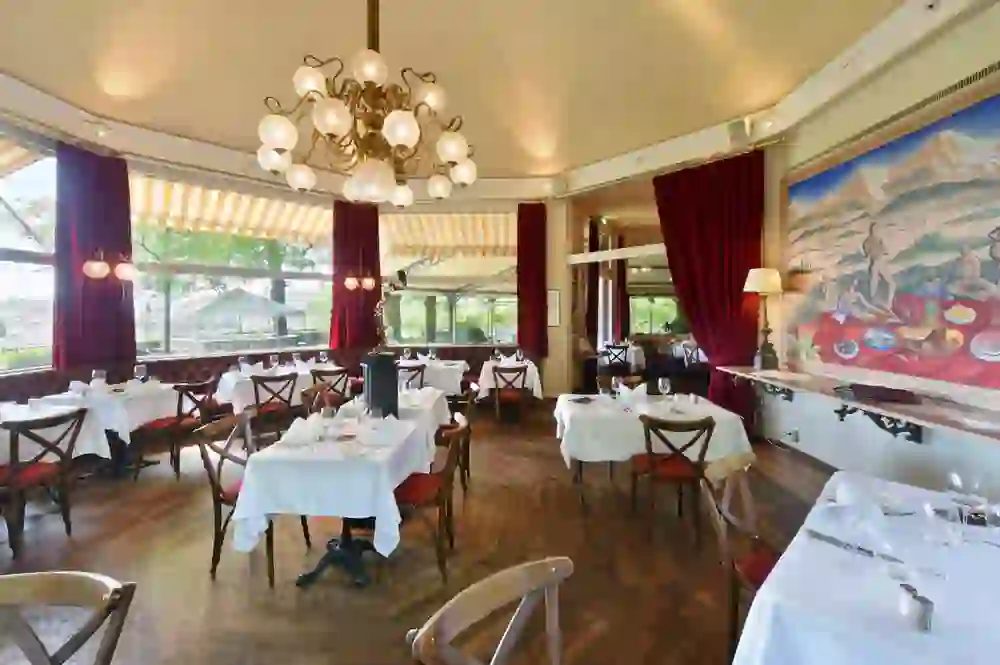 L'immagine mostra la luminosa sala da pranzo della Josephine Brasserie dell'Hotel Unique Innere Enge, che trasmette una sensazione di classica eleganza e distinta ospitalità con i suoi eleganti lampadari e i pittoreschi murales.