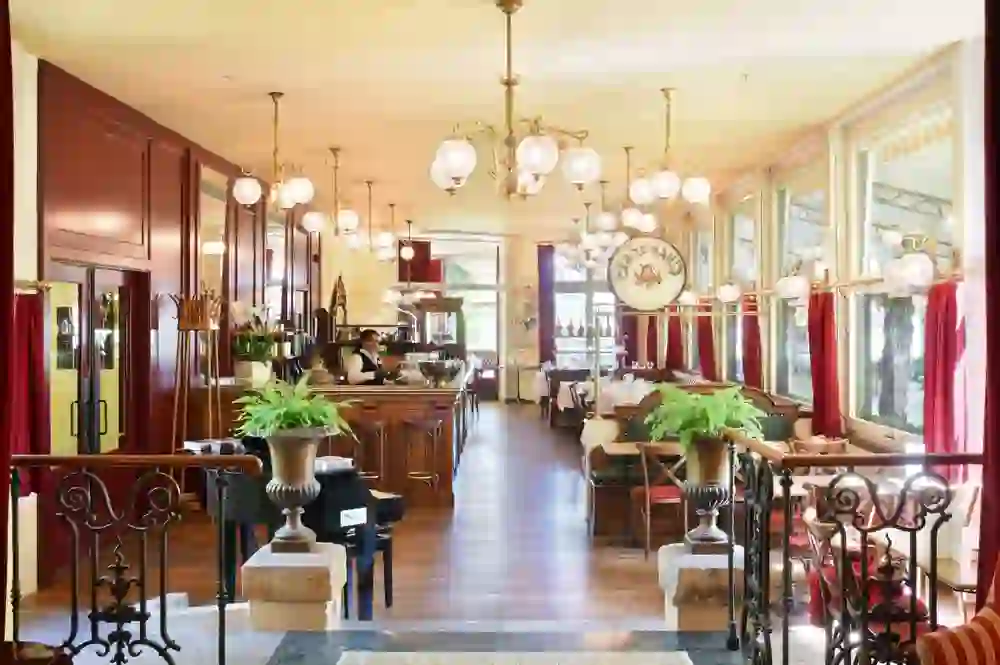 La foto presenta la Josephine Brasserie dell'Hotel Unique Innere Enge con un tocco di fascino nostalgico, catturato dai classici mobili in legno e dalle eleganti tende rosse che creano un'atmosfera calda e invitante.