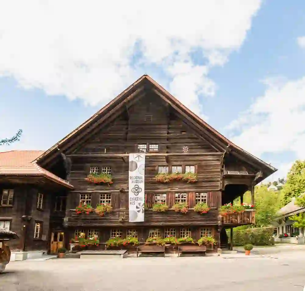 Das charmante Regionalmuseum Chüechlihus in Langnau, ein traditionelles Holzhaus, präsentiert sich gastlich mit blühenden Fensterläden unter einem strahlend blauen Himmel.