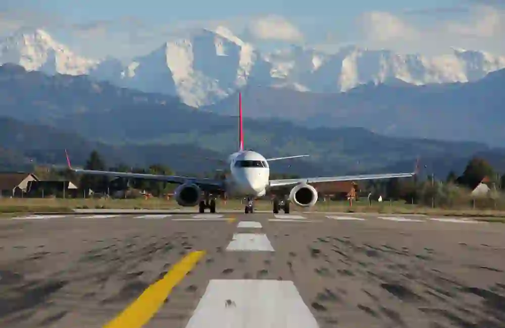 Ein Flugzeug steht am Start auf der Landebahn des Flughafens Bern-Belp, im Hintergrund die majestätische schneebedeckte Eiger, Mönch und Jungfrau - ein Moment des Staunens und der Reiselust.