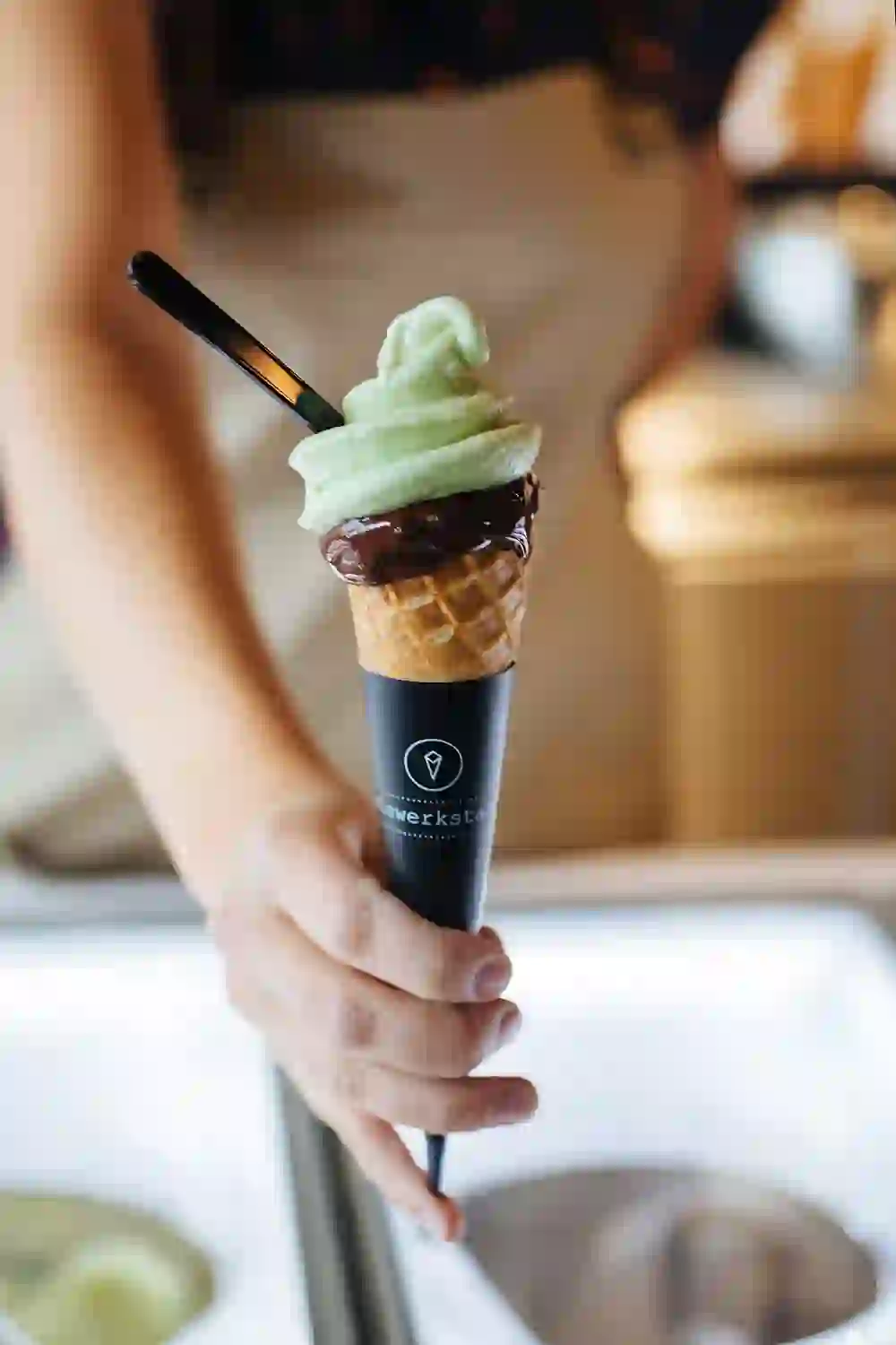 An appetising ice cream with a green waffle and chocolate coating is presented in the ice cream parlour at the old tram depot. The scene radiates freshness and enjoyment, perfect for a sweet break on a sunny day.