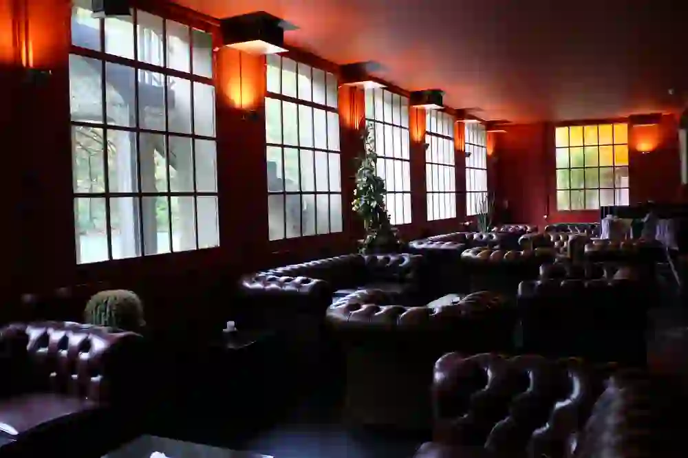 La photo montre un café stylé, meublé de canapés en cuir sombre, dont l'éclairage chaleureux crée une ambiance confortable et détendue.