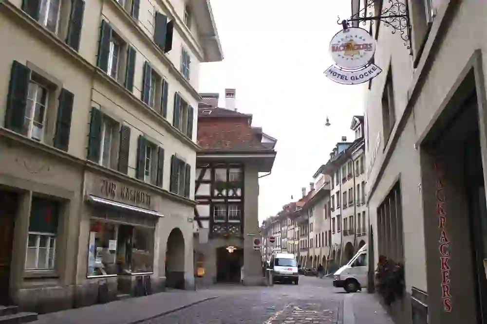 The picture shows an alley in the city of Bern and the entrance to the Bern Backpackers Hotel Glocke can be seen on the right. In the background you can see cross-country ski tracks and the street is paved. The alley is part of the old town centre.
