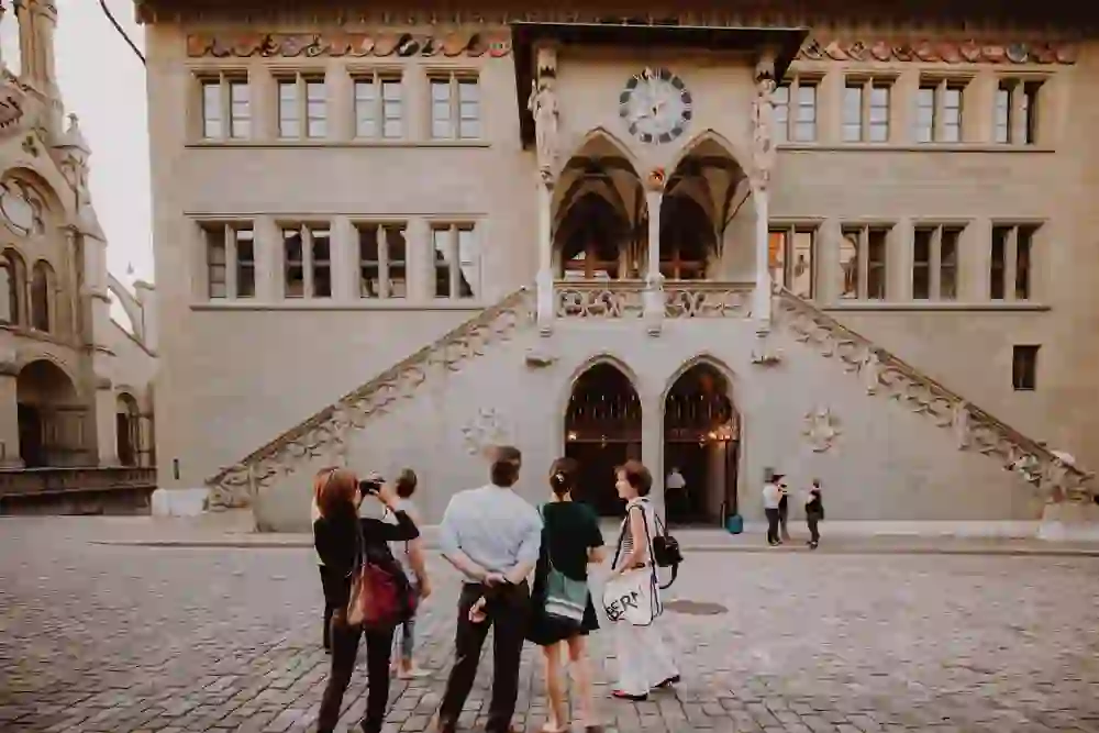 The city tour group looks intently at the architecture of a historic building in Bern, surrounded by an ambience of admiration and learning, while the gentle dusk emphasises the experience.