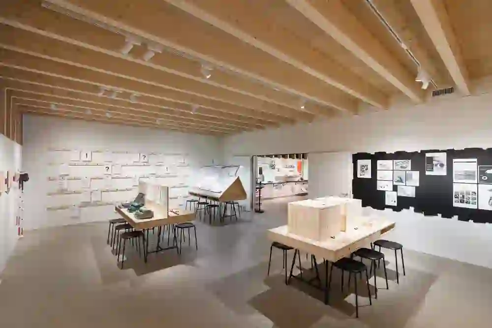 Das Bild zeigt einen hellen, modern gestalteten Ausstellungsraum des Schweizerischen Blindenmuseum mit einer Holzdecke und zahlreichen Exponaten auf Tischen und an Wänden. Auf einer Wand sind Grafiken oder Fotos präsentiert, während im Raum verschiedene Modelle und interaktive Stationen zu sehen sind. Die Atmosphäre erscheint ruhig und informativ, mit einem Fokus auf Bildung und Entdeckung.