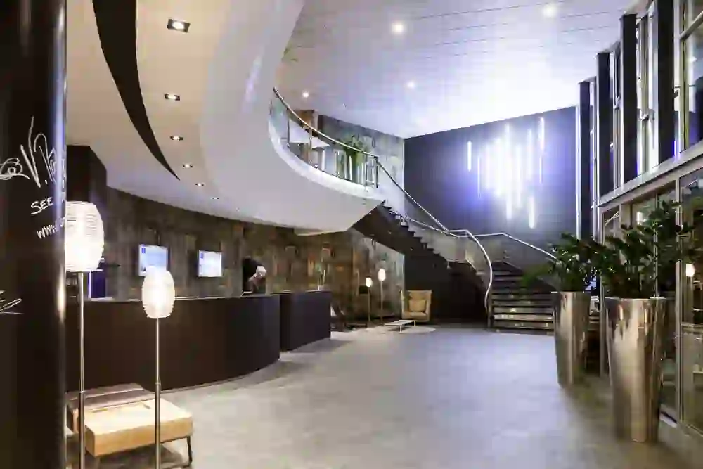 The picture shows the lobby of the Novotel Bern Expo with a modern, elegant design. The curved staircase and dynamic lighting create a sense of movement and contemporary comfort that invites visitors into a world of modern hospitality.