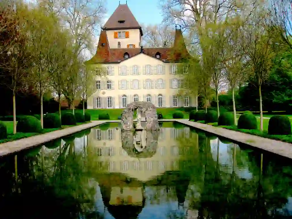 The magnificent Jegenstorf Castle is reflected in a calm mirror of water, framed by a perfectly trimmed garden. The symmetry and peaceful tranquillity lend the scene a fairytale aura.