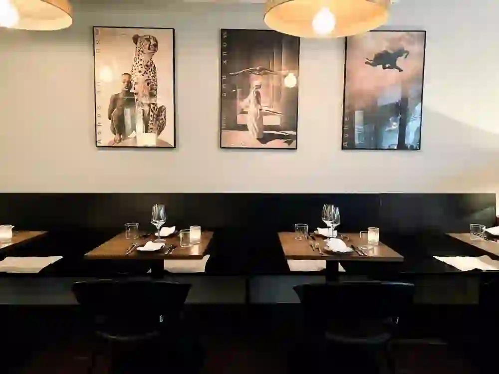 L'immagine mostra un angolo elegante del ristorante Bonbec. L'arredamento semplice con mobili scuri, bicchieri da vino pregiati e una sottile luce di candela creano un'atmosfera calma ed elegante. Alle pareti sono appese fotografie artistiche che danno un tocco personale alla sala. Ideale per una cena rilassata in un ambiente moderno e urbano.