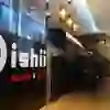 The picture shows the interior of the Oishii Sushi & Grill restaurant in Bern. The atmosphere is inviting and modern, with stylish lighting and an elegant interior. A person sits relaxed in the background, which conveys a calm and cosy mood.