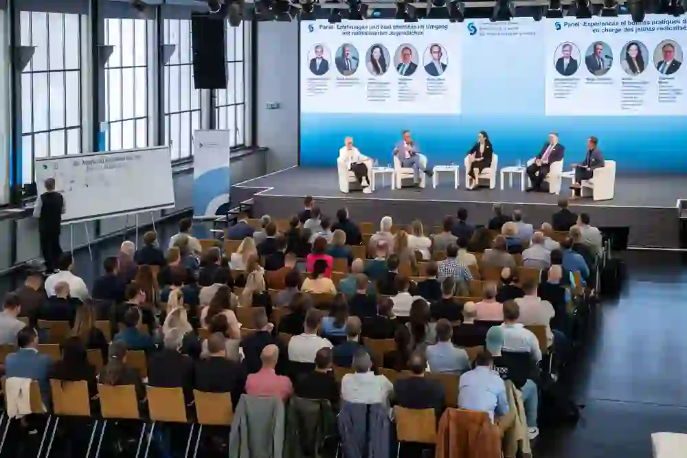 A well-attended symposium: A panel discusses current topics on stage, the audience listens intently. The objective atmosphere is characterised by attention, exchange and a shared interest in sound solutions.