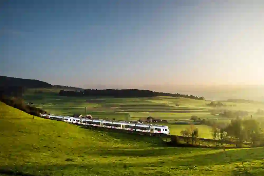 Il treno Kambly si snoda attraverso la pittoresca valle dell'Emmental, con il sole al tramonto che bagna il paesaggio di una luce soffusa. La scena incarna la tranquillità e la bellezza della natura.