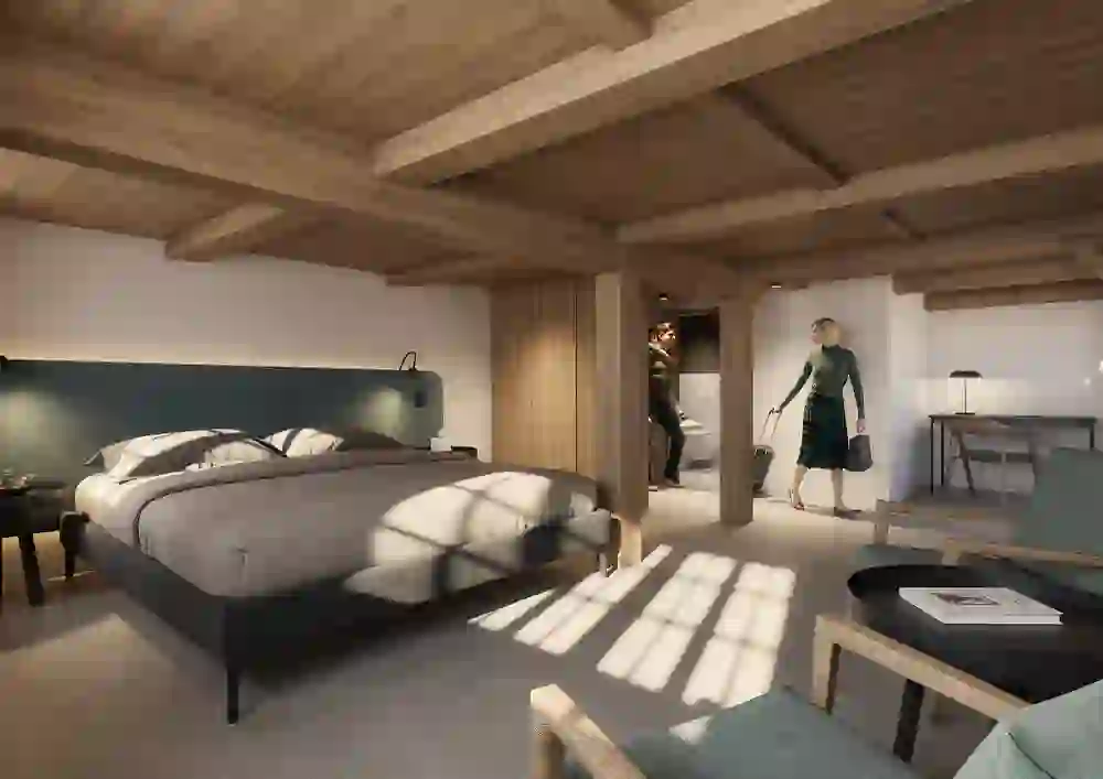 The picture shows a modern **hotel room** with lots of wood and a warm ambience. A large, comfortable bed with an elegant headboard is in the foreground, next to a small table with armchairs. Wooden ceilings and walls create a cosy, natural atmosphere. In the background, guests are just entering the room, which emphasises the inviting atmosphere. A desk with lamp completes the furnishings - ideal for a relaxing or business stay.