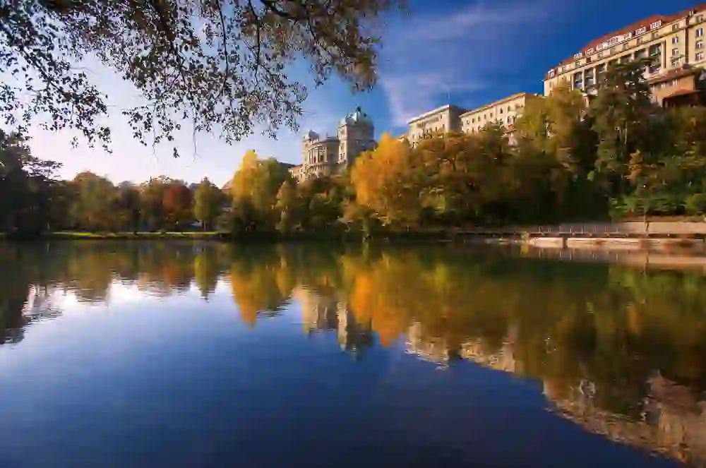 The autumnal splendour is reflected in the waters of the Aare, while the Federal Palace in Bern stands in the gentle autumn sun, creating an atmosphere of peace and beauty.
