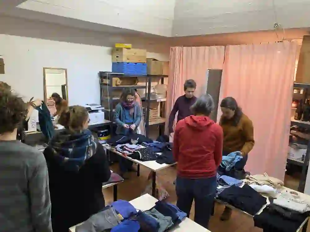 Das Bild zeigt einen Kleidertausch der Foodcorp Güter. Menschen stöbern entspannt durch die Kleidung, tauschen Stücke aus und tauschen sich aus. Eine gemütliche, gemeinschaftliche Atmosphäre herrscht, geprägt von Nachhaltigkeit und dem Wunsch nach bewussterem Konsum.