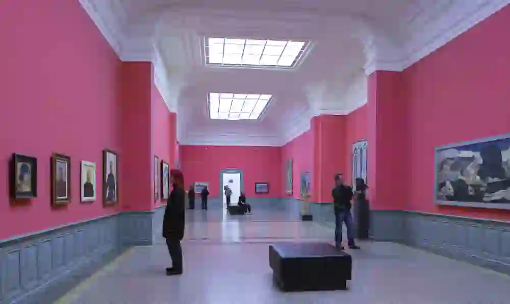 In this vibrant room at the Kunstmuseum Bern, the bold pink wall colour stands out, drawing the eye to the portraits and artworks on display. Natural light floods the room, creating a friendly atmosphere and emphasising the magnificent ceiling structure. Visitors contemplate the collection, surrounded by a sense of modern creativity and historical architecture.