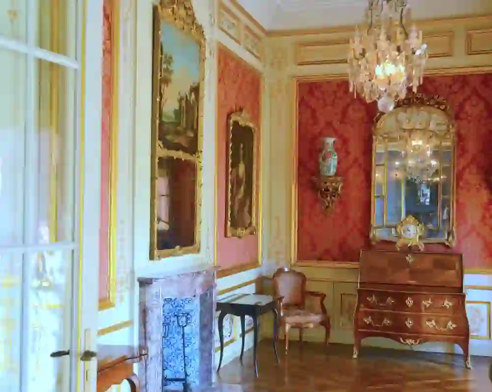 The magnificent interior of Jegenstorf Castle reveals itself in a room with vivid red walls, gold-decorated paintings and a classic chandelier that radiates elegance and rich history.