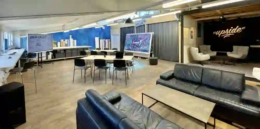 Salle d'atelier ouverte avec des tables, des chaises, un tableau blanc et des murs créatifs. L'environnement semble vivant et moderne, empreint d'échanges, de travail d'équipe et d'énergie créative.