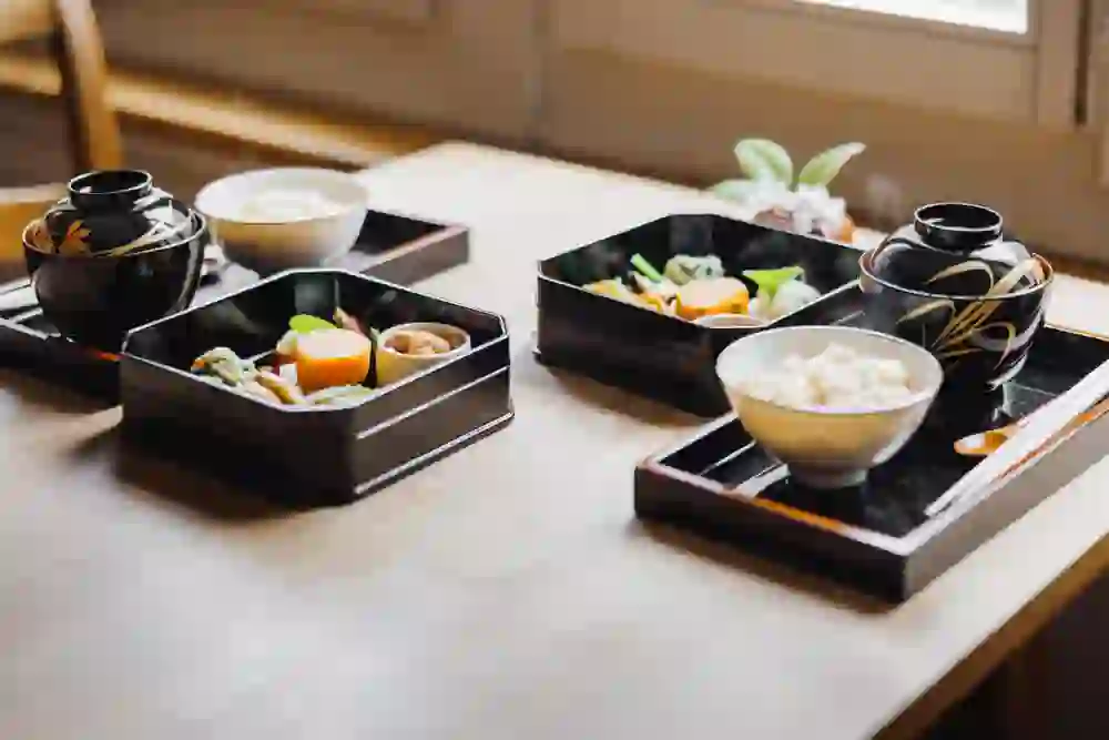 Das Bild zeigt einen japanisch angehauchten Frühstückstisch. Mit schwarzem Geschirr, dass goldenen Verziehrungen enthält. Der Raum ist hell und einladend