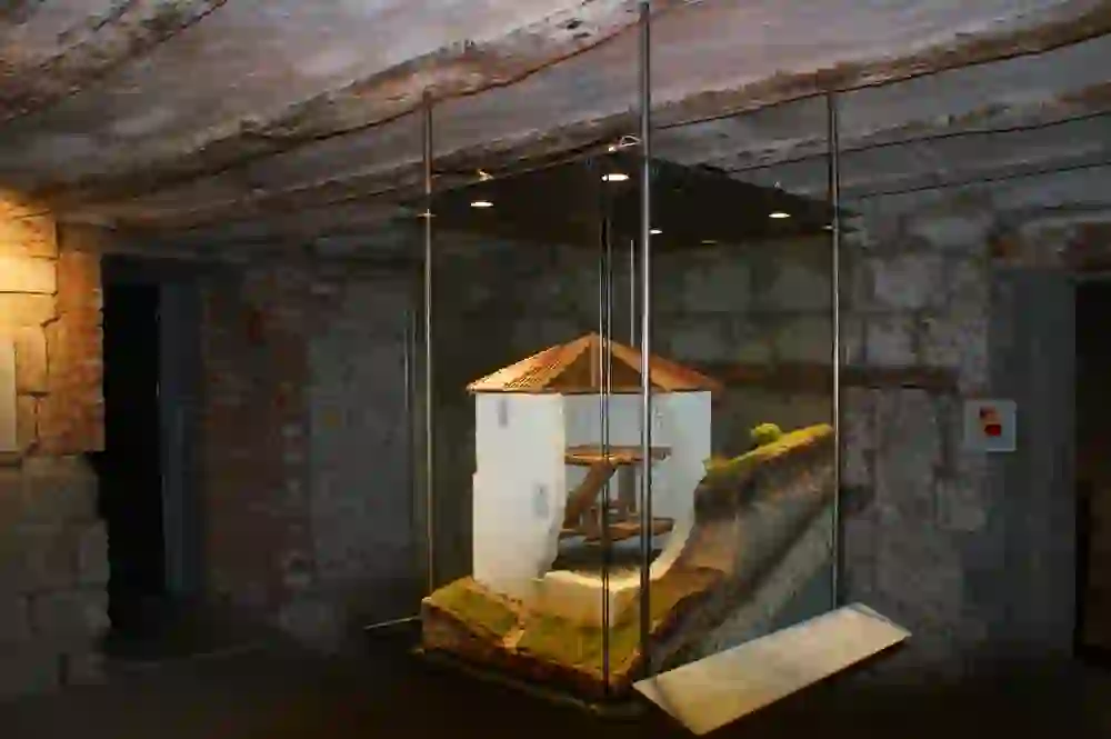 The picture shows a model of a historic fountain, the Lenbrunnen, displayed in a room with rustic architecture, possibly within a museum or information centre. The lighting and the protective glass cover emphasise the model.