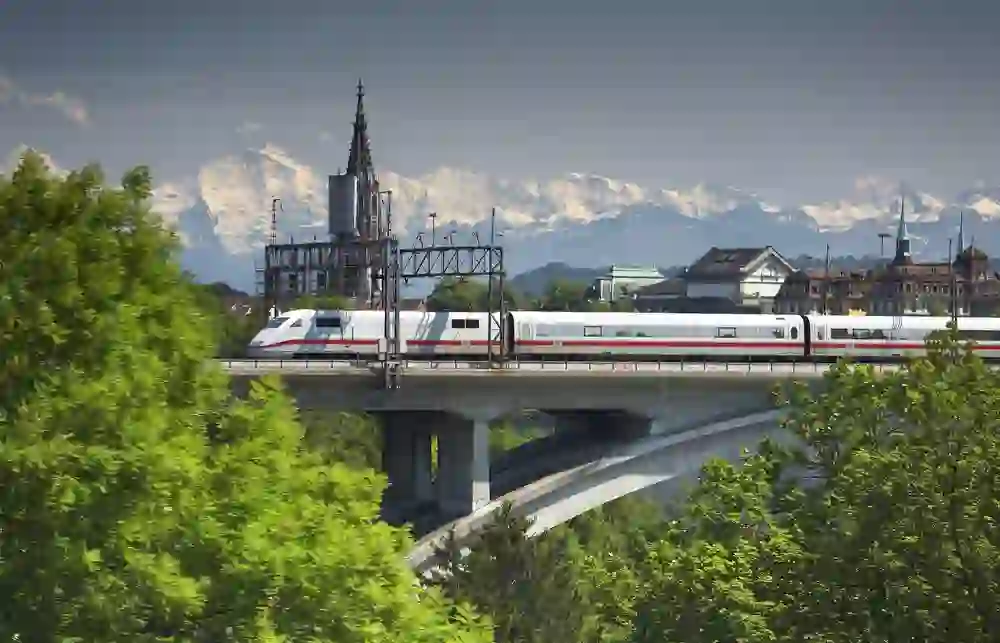 Un train à grande vitesse traverse un pont devant la silhouette de Berne, encadrée par les majestueuses Alpes enneigées, qui dégagent une dynamique silencieuse.