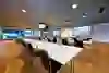 A stylish meeting room with a large table facing a screen that displays "Welcome". Behind the floor-to-ceiling windows there is a view of a stadium, the atmosphere is exclusive and ready for an event.