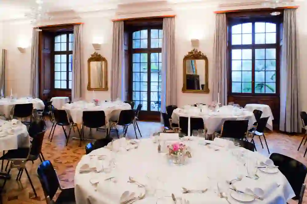 Das Bild zeigt einen eleganten Speisesaal im Schloss Münchenwiler, mit fein gedeckten Tischen unter stilvollen Kronleuchtern. Die geschmackvolle Einrichtung und das warme Licht schaffen eine atmosphärische und festliche Stimmung.